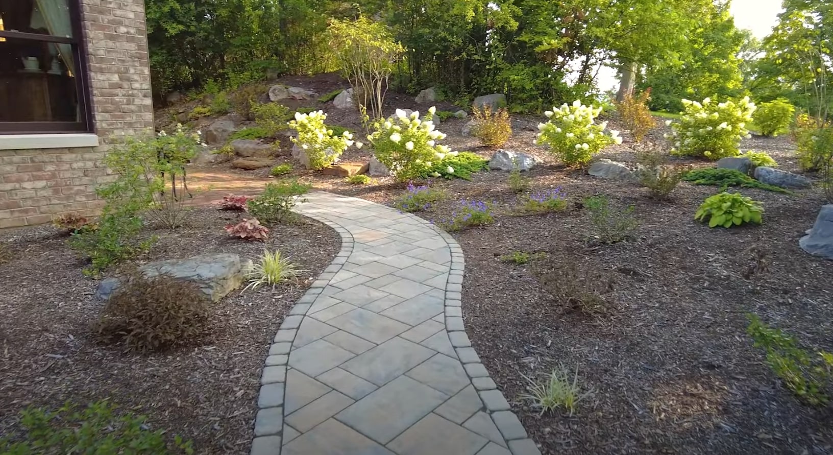 Custom stone pathway design with professional plant installations Professional landscaping with curved stone pathway and mulched garden beds in Doral
